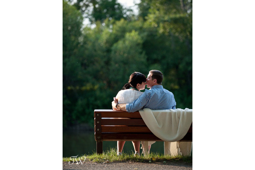 couple kiss on a park bench during their summer engagement session captured by Tara Whittaker Photography