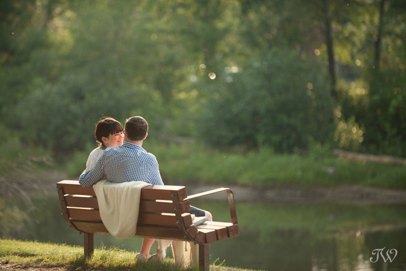 couple sit on a park bench during their engagement session on the Elbow River