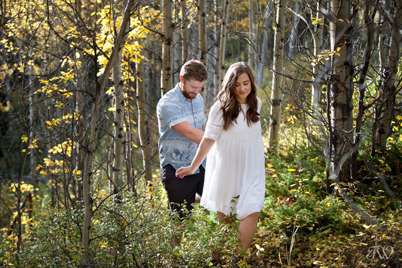 bride and groom walk through the woods during their fall engagement session