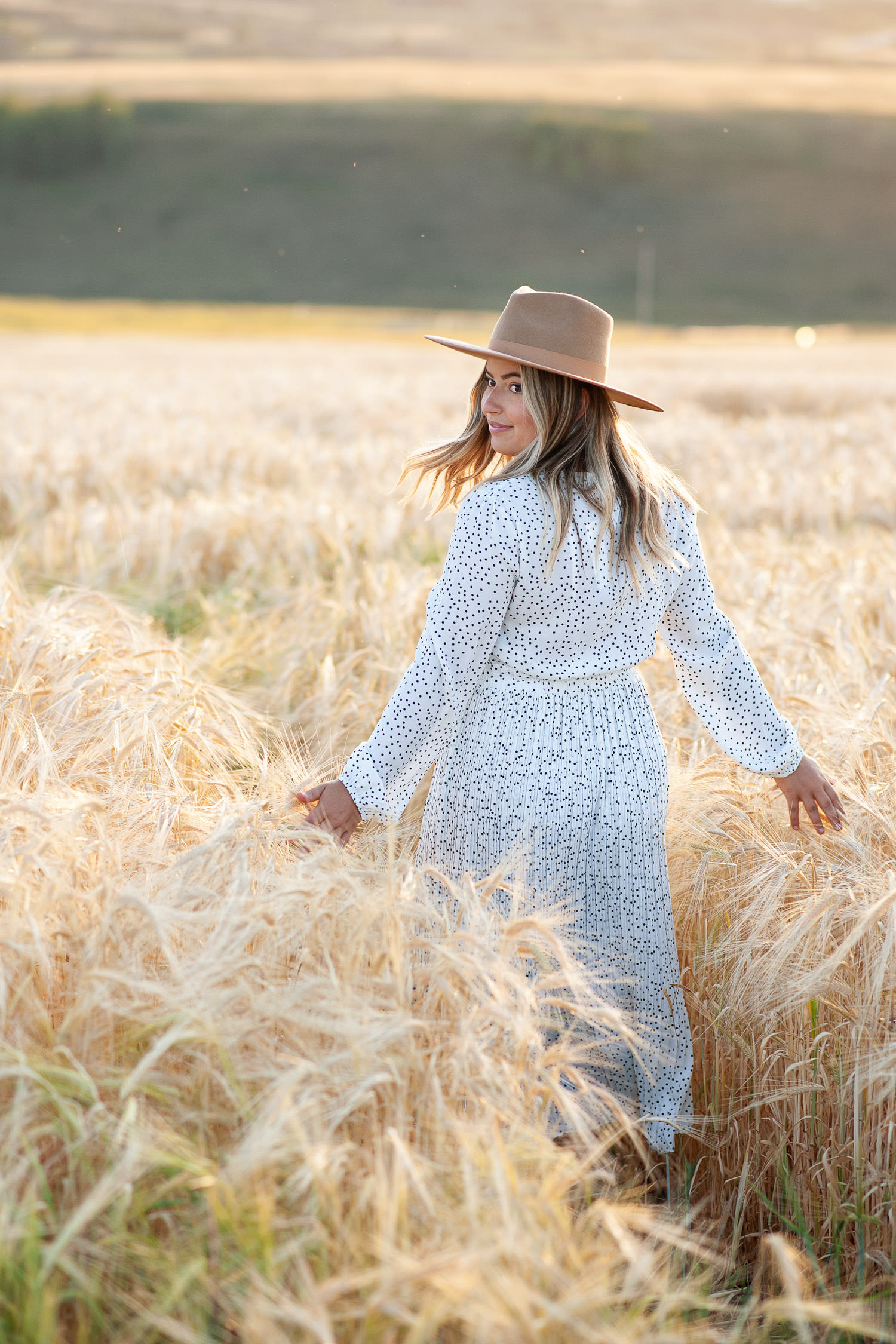 bride walks through a field of barley captured by Tara Whittaker Photography